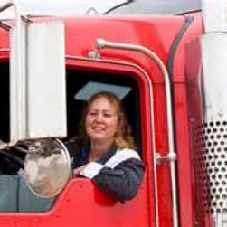 Woman Truck Driver leaning out of the driver side window smiling.