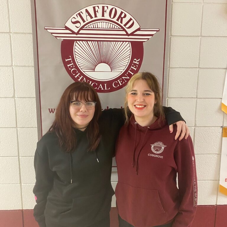 Gabby and Emma stand arm in arm. Both are smiling.