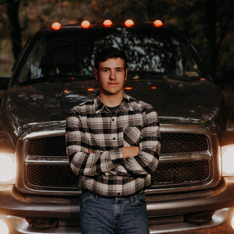 Eli stands in front of a truck and has a slight smile on his face