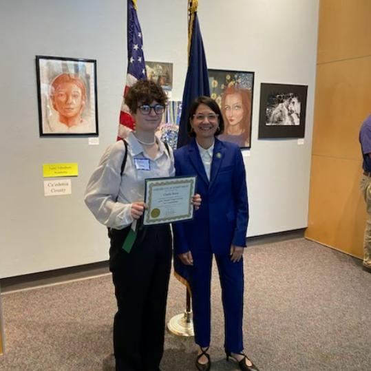 Charlie stands with a paper award and a ribbon in front of art hanging on the wall behind