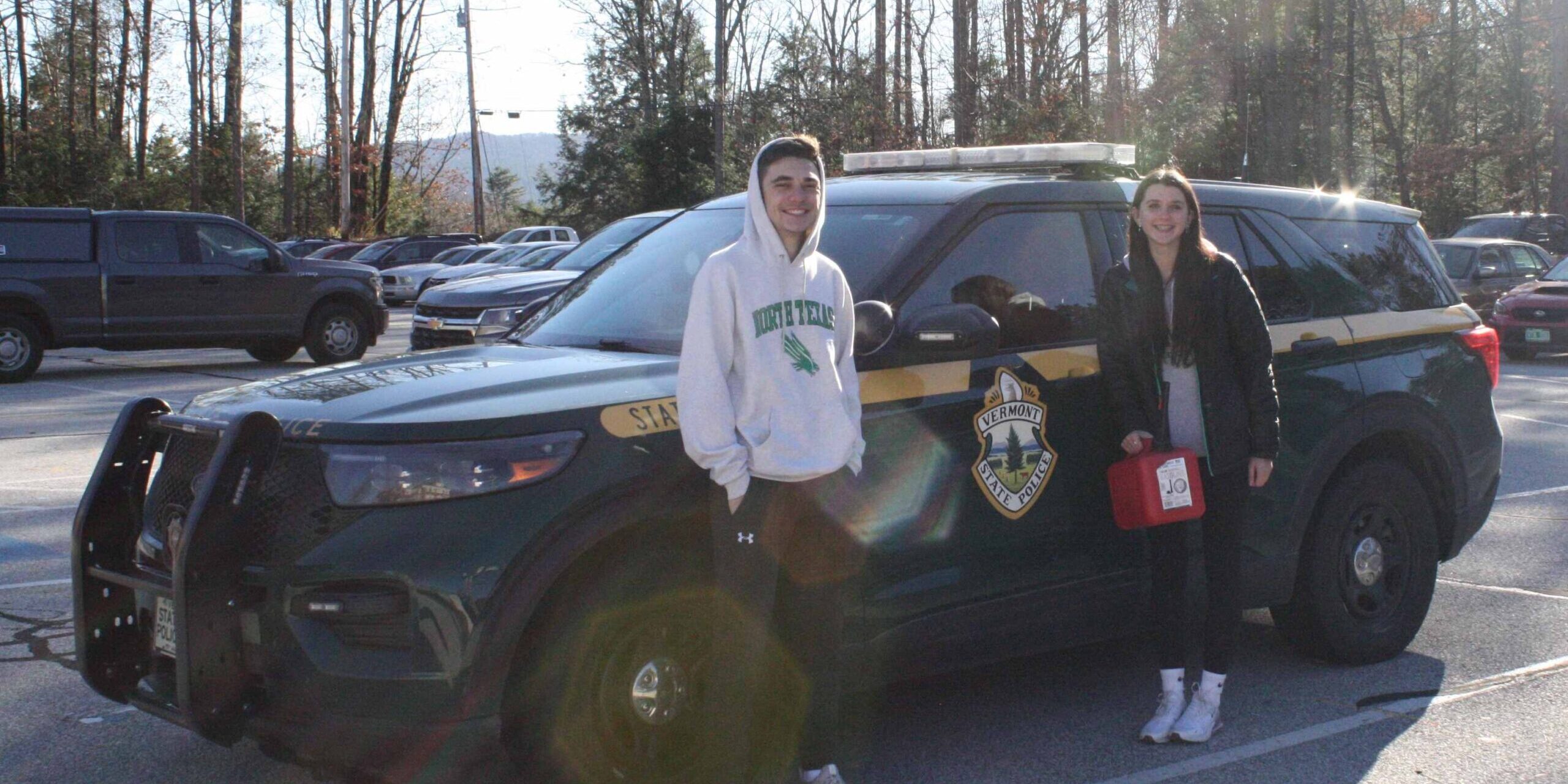 Two students stand by a Vermont State Police vehicle.