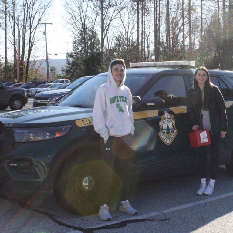 Two students stand by a Vermont State Police vehicle.