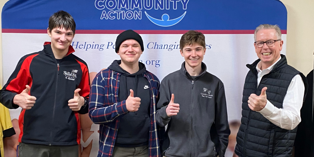 three students give thumbs up in front of a BROC sign with Director Tom Donahue