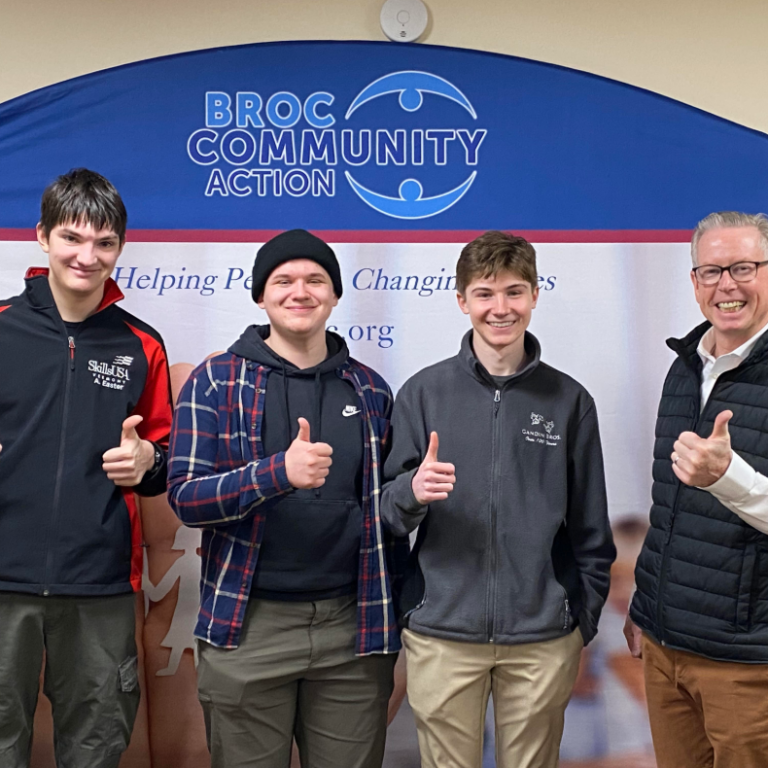 three students give thumbs up in front of a BROC sign with Director Tom Donahue