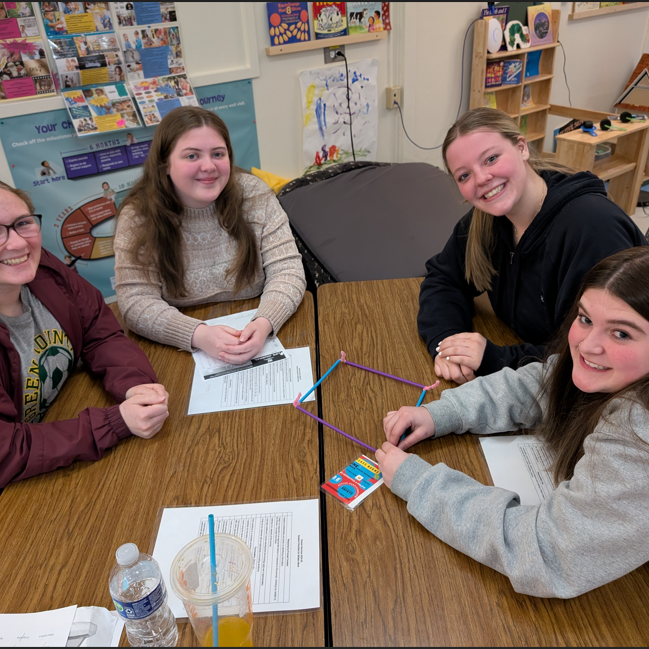 Four students smile at the camera as they sit at a table