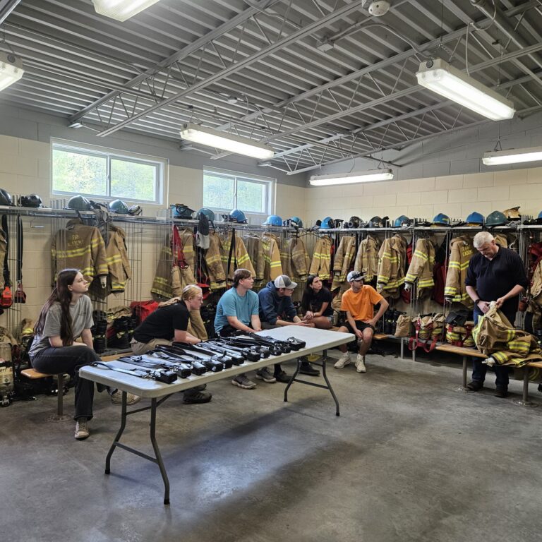 Students sit on a bench surrounded by fire fighting equipment