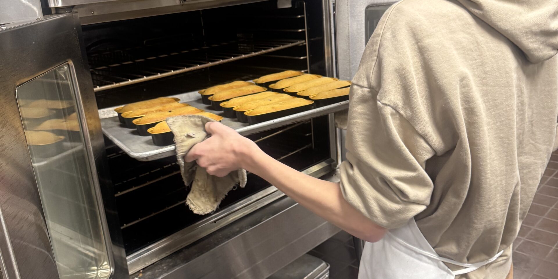 A student is pulling a tray of baked items out of an oven. We can only see the side of his body and face