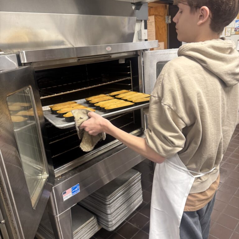 A student is pulling a tray of baked items out of an oven. We can only see the side of his body and face
