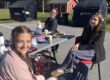 Three students sit around a table. All are smiling at the camera, the table has face painting materials.