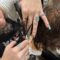 close up of hands holing hair and a student using shears to trim the hair