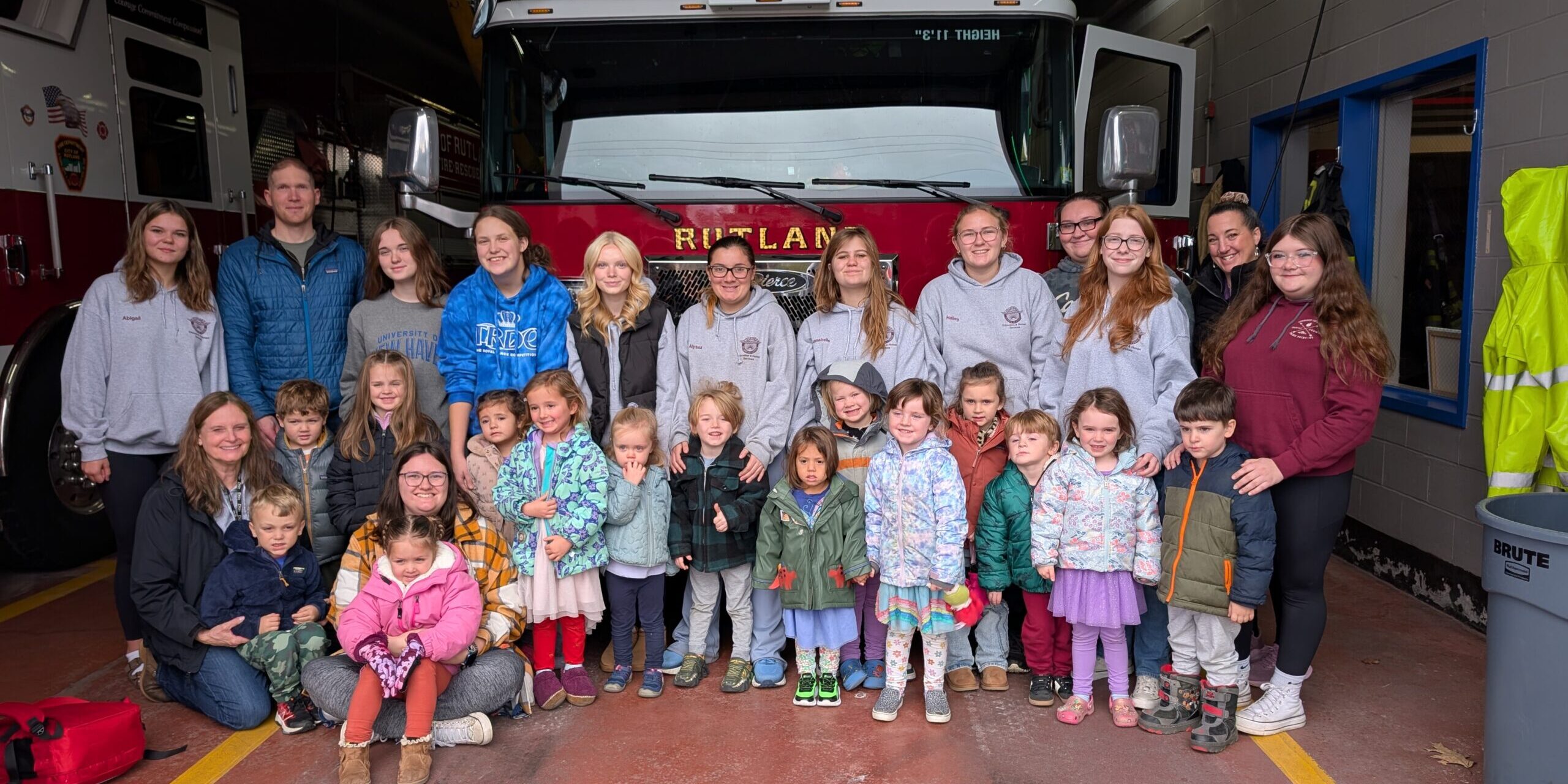 a group of preschoolers and high school students stand in front of a firetruck
