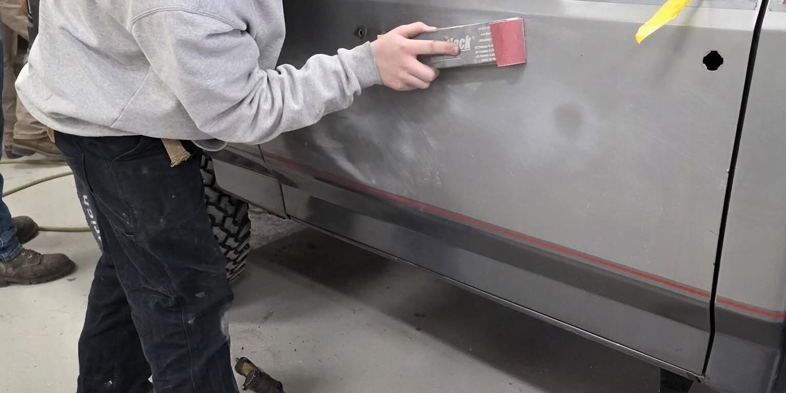 15179 – Scott Herdling (1) A student uses a long sanding device on the door of a truck