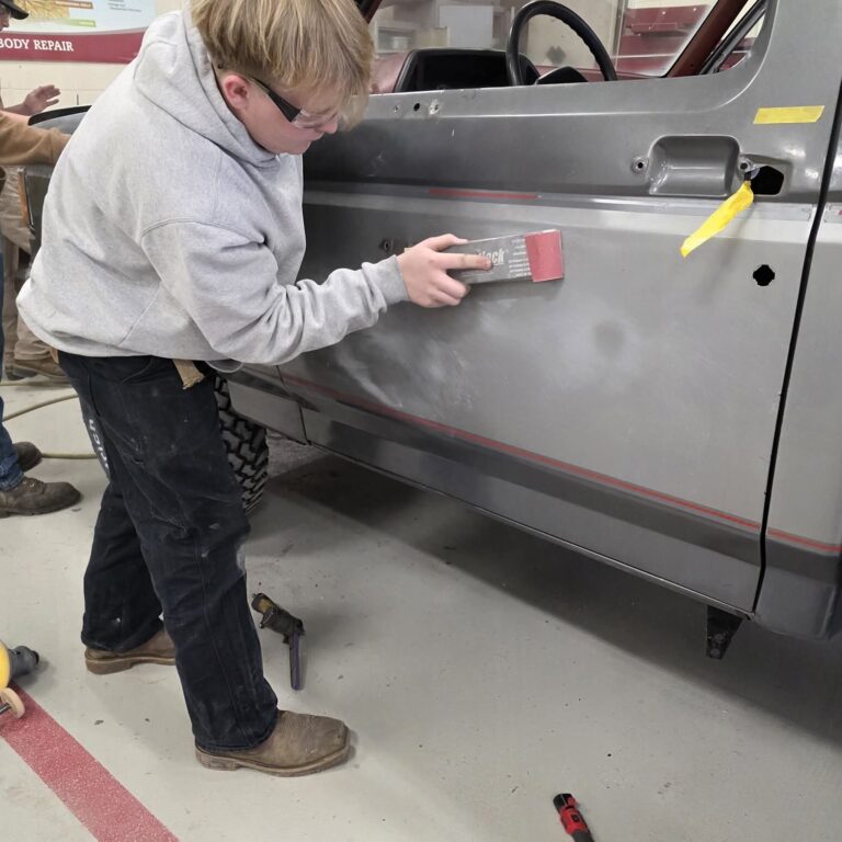 15179 – Scott Herdling (1) A student uses a long sanding device on the door of a truck
