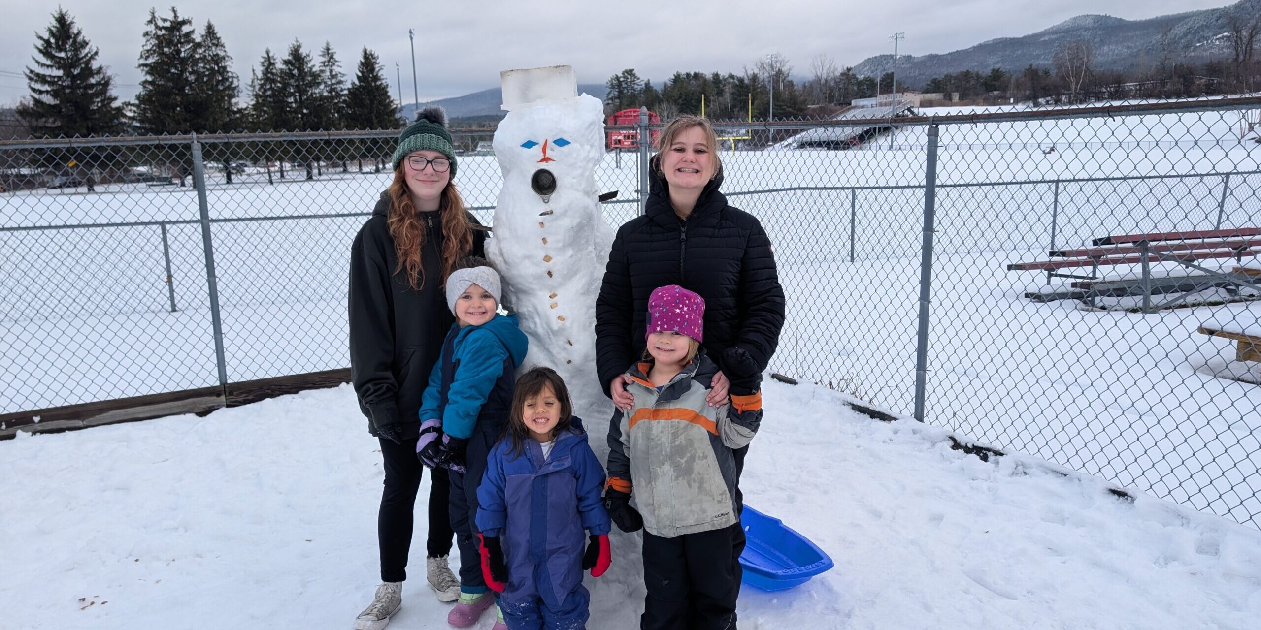 3 preschoolers gather around a snowman with two adults
