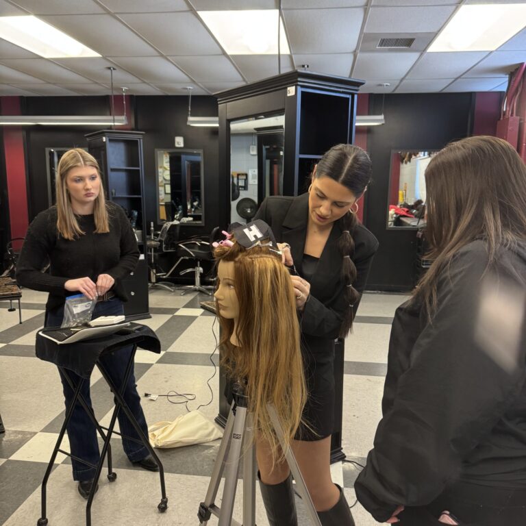 Paige attaches a hair extension to a manikin head