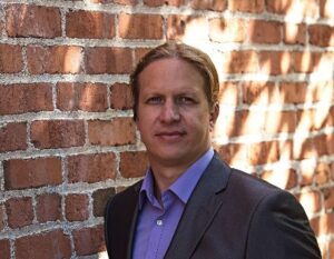 Steve stands in front of a sunlit brick wall