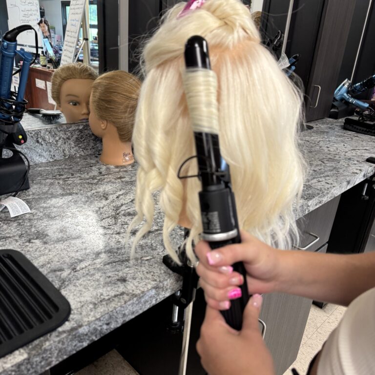 IMG_1363 – Stacy Hutchins A student's hands are shown using a curling iron to produce ringlet curls on a mannikinhead